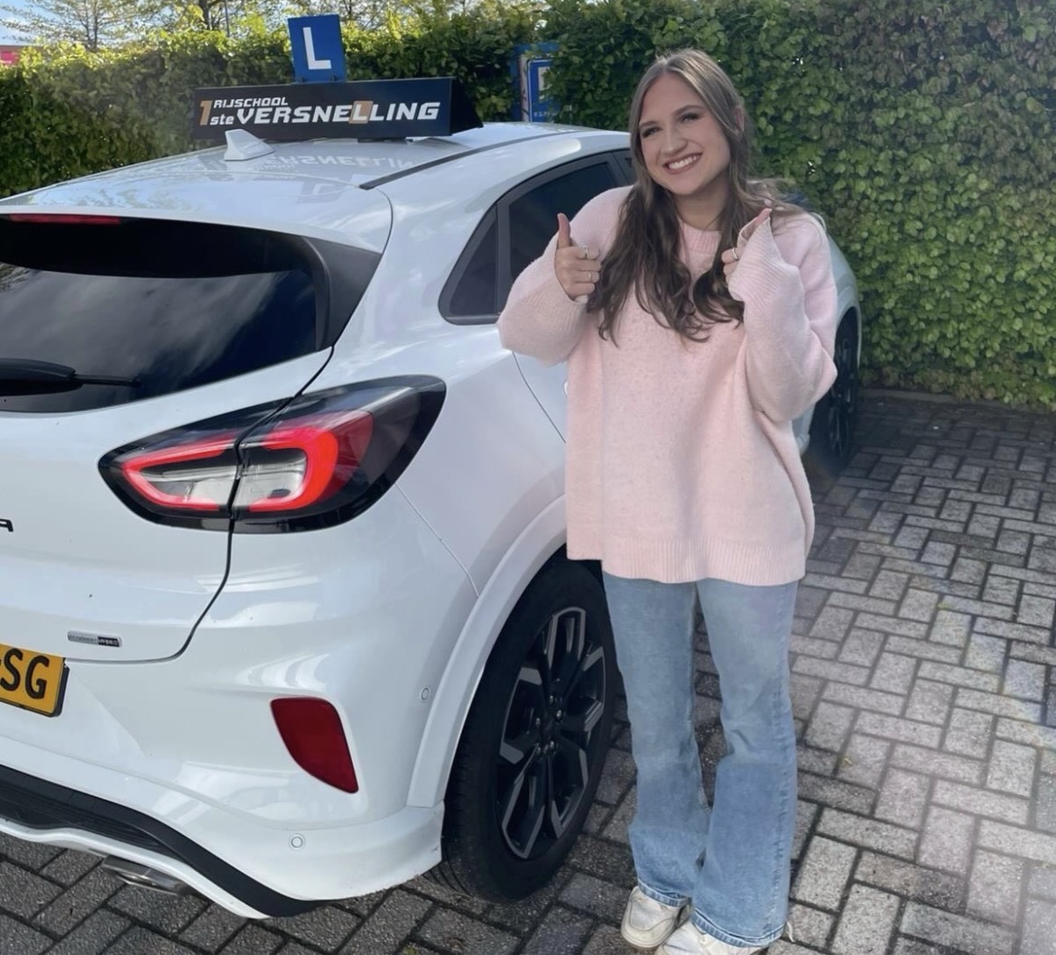 Geslaagde leerling lachend naast de witte lesauto