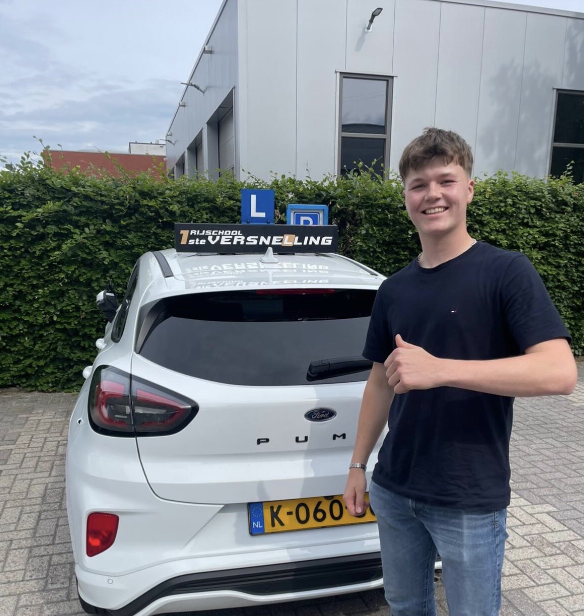 Geslaagde leerling met duim omhoog naast de lesauto