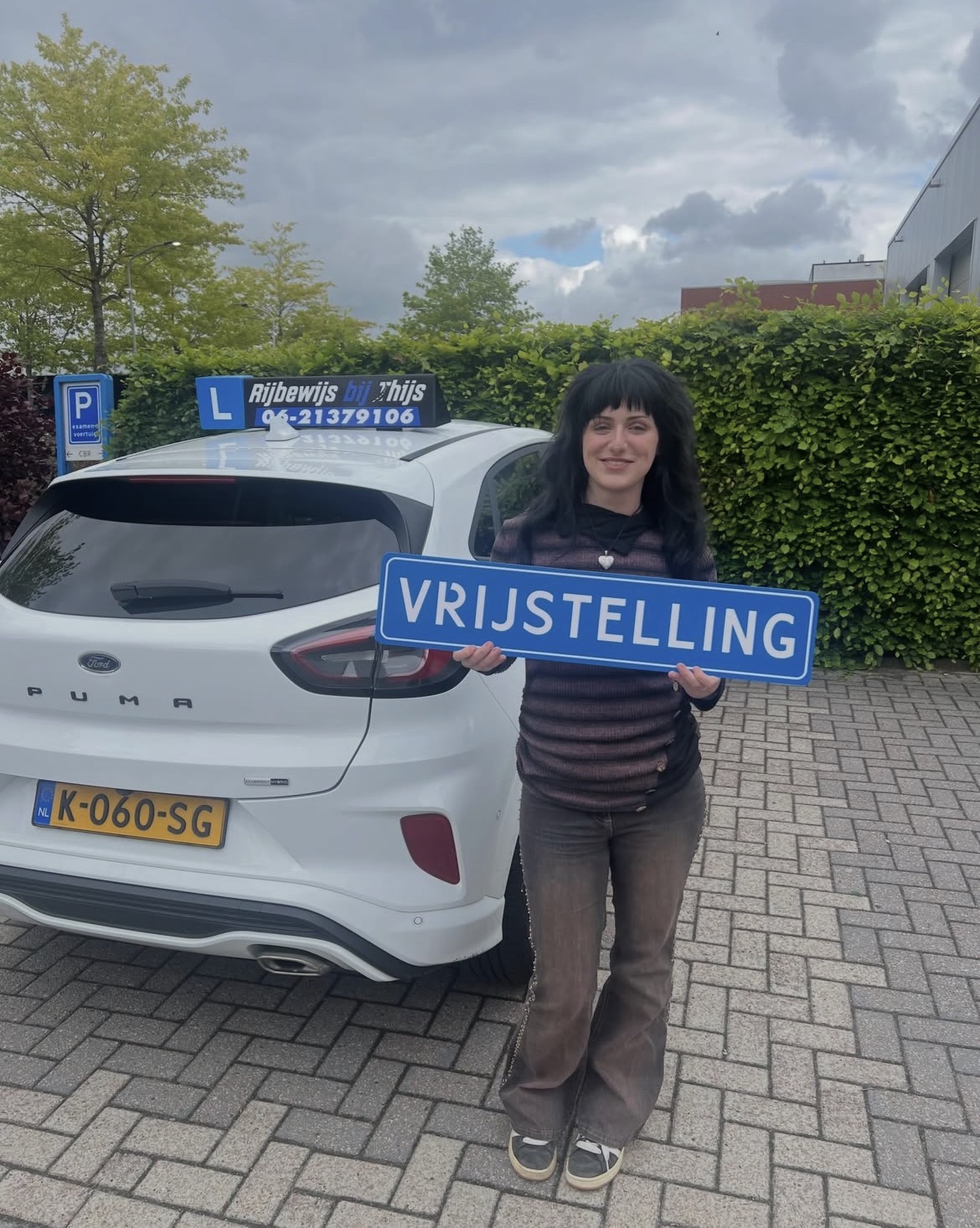 Geslaagde leerling met het bord Vrijstelling naast de lesauto van Rijbewijs bij Thijs